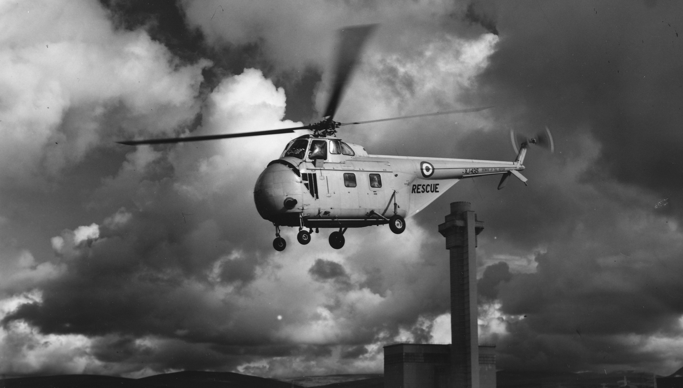 A helicopter of the Royal Air Force taking air samples during the 1957 Windscale fire, with one of the reactors in the background. Image courtesy of Louise Rawling.