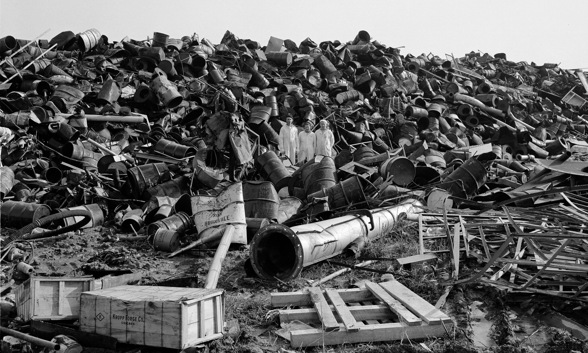 Three production workers stand in a scrap pile at the Feed Materials Production Center, January 5, 1956. Courtesy of the U.S. Department of Energy, flickr.com.